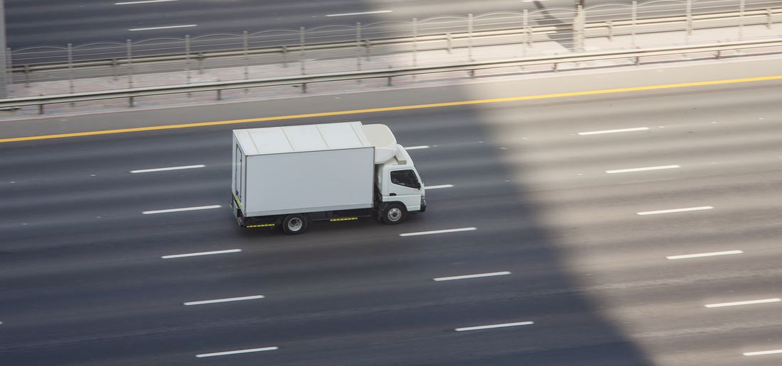 A white box truck driving along a multi-lane highway, seen from above