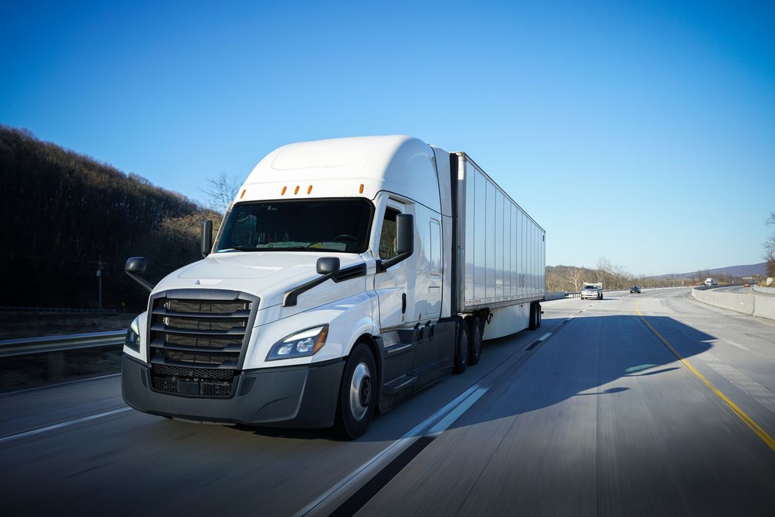 A white semi truck and trailer on a highway under a clear sky