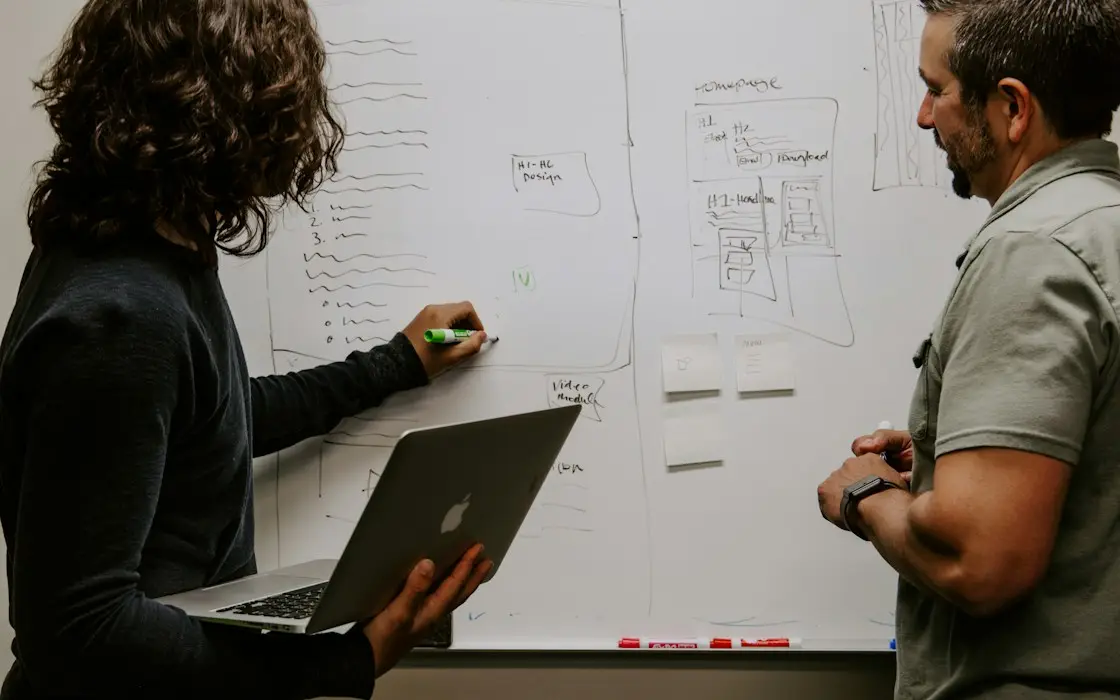 Two colleagues mapping a plan on a whiteboard, one holding a laptop